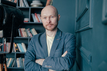 Portrait of attractive adult successful bald man with beard in suit against books wall