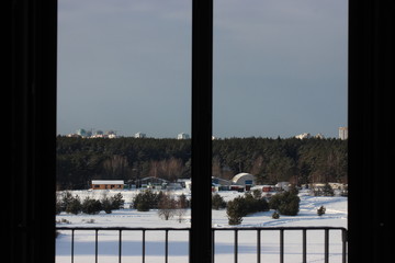 view of the winter countryside and forest, high-rise buildings in the distance and construction cranes, clean snow on a Sunny day. the rest of the window