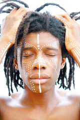 Portrait of young african man with dreadlocks and traditional face paint, hands pulling his hair