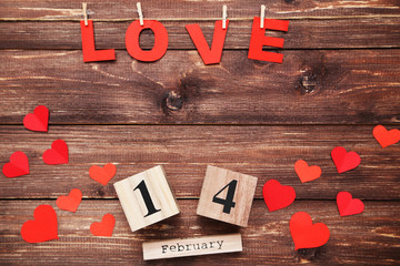 Word Love with paper hearts and wooden calendar on brown table