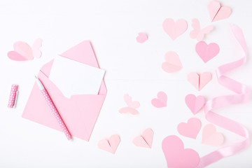 Pink paper hearts with envelope and pen on white background