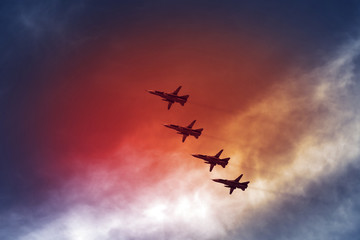 Combat aircraft fighters fly against the red fire sky. Jet squadron