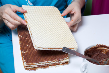 Cooking waffle cake. A woman puts a stack of wafer cakes, smeared with a mixture of cocoa and butter. Alternately with wafer cakes, smeared with boiled condensed milk.