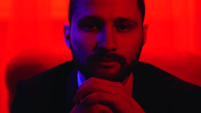 Portrait of bearded man leans forward sitting in his chair. Shooting in red light