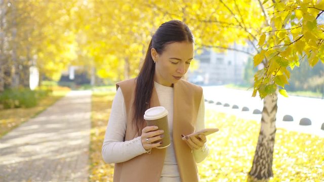 Fall concept - beautiful woman drinking coffee in autumn park under fall foliage