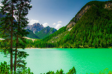Lake Braies in the Dolomites mountains, a cloudy summer day, seen from the green forest, during a trek