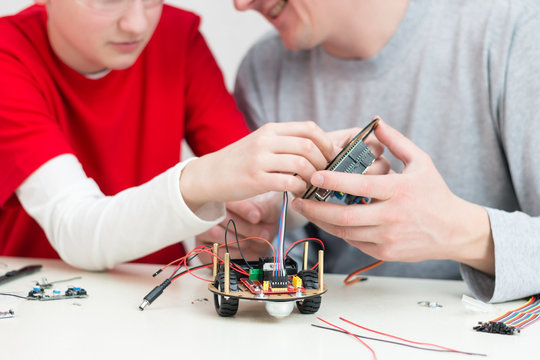 A teenager boy with his dad teacher collects a handmade robot working on the arduino platform. STEM education for children and teenagers, robotics and electronics. DIY. AI. STEAM.