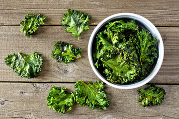 Bowl of healthy kale chips. Top view, on a rustic wood background. - obrazy, fototapety, plakaty