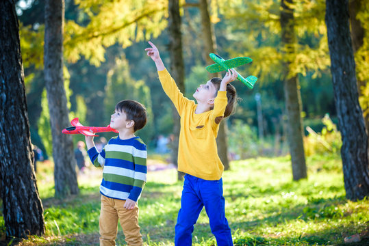Happy two brother kids playing with toy airplane against blue summer sky background. Boys throw foam plane in the forest or park. Best childhood concept