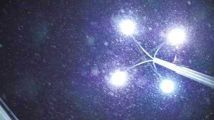 Heavy snow falling in winter city, illuminated by street light. Dark sky in background. Slow motion.