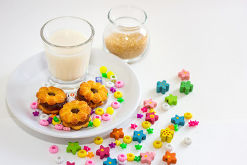 Milk with cookies on dish and brown sugar in jar with little toy around on with background
