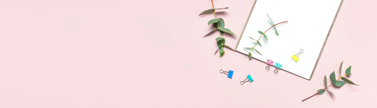 Flat lay clipboard with blank paper, green eucalyptus branches on pastel pink background. Top view female office workspace minimal mock up template concept, copy space. Feminine floral desktop