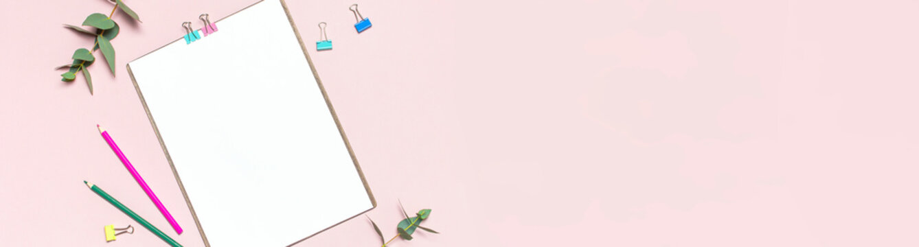 Flat lay clipboard with blank paper, colour pencils, clips, eucalyptus branches on pink background. Top view female office workspace minimal mock up template concept copy space Feminine floral desktop