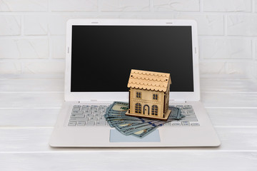 Wooden house model with dollar banknotes on laptop keyboard