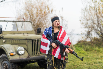 Woman with american flag and rifle near military car