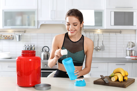 Young woman preparing protein shake at table in kitchen