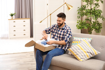 Fototapeta premium Young man opening parcel on sofa at home