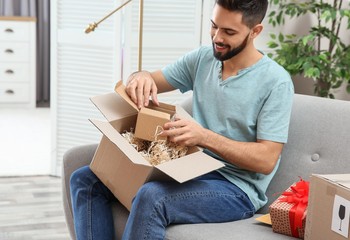 Young man opening parcel on sofa at home