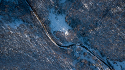 Curvy windy road in snow covered forest, top down aerial view.