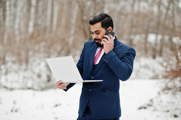 Stylish indian beard business man in suit posed at winter day outdoor with laptop at hands,...