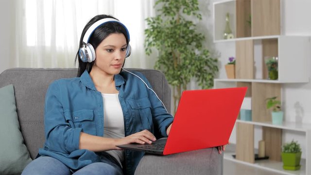 Serious woman with headphones browsing laptop content sitting on a couch at home