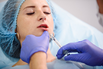 Fototapeta premium girl do plastic operation in medical clinic; doctor does lip augmentation surgery; injecting operation on lips