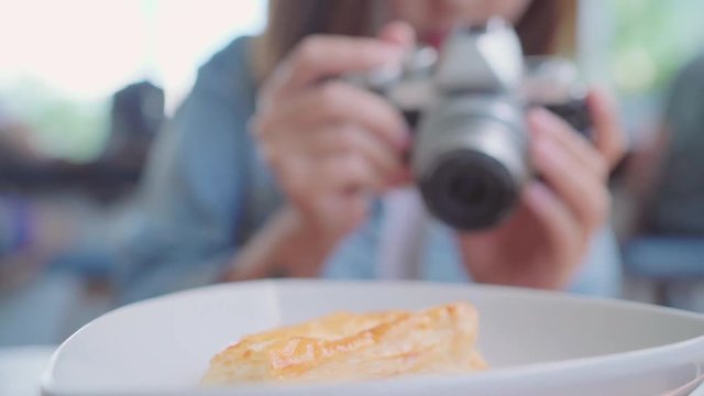 Food blogger Asian woman using camera for photo dessert, bread and drink while sitting on table in cafe. Lifestyle beautiful women relax at coffee shop concepts.
