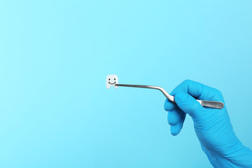 Dentist holding small plastic tooth with tweezers on color background. Space for text