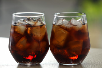Glasses of cola with ice on table against blurred background