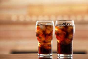 Glasses of cola with ice on table against blurred background. Space for text