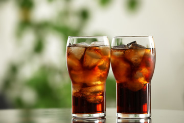 Glasses of cola with ice on table against blurred background