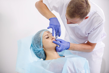 girl do plastic operation in medical clinic; doctor does lip augmentation surgery; injecting...