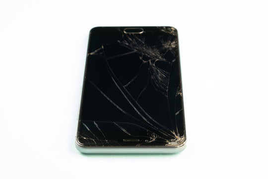 Mobile phone with broken black screen, top view. Distressed damaged smartphone in pale green background, shallow depth of field