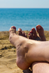 view of the female legs sitting girl on the beach by the sea