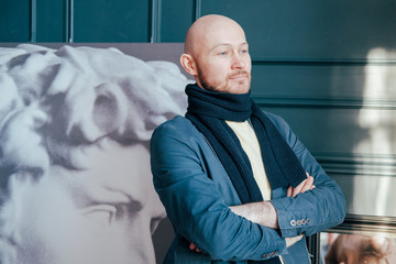Portrait of attractive adult successful bald man art critic historian with beard in scarf in art...
