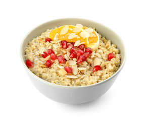 Bowl of quinoa porridge with nuts, orange and pomegranate seeds on white background