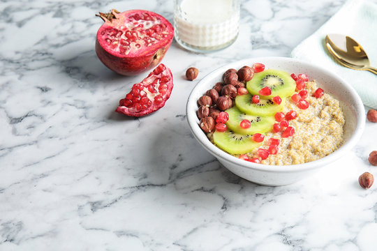 Bowl of quinoa porridge with hazelnuts, kiwi and pomegranate seeds served for breakfast on marble table. Space for text