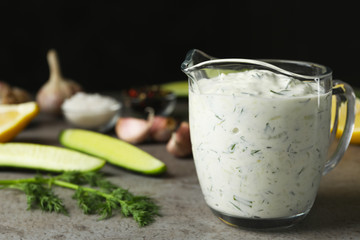 Glass jug of Tzatziki cucumber sauce with ingredients on table. Space for text
