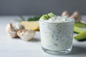 Glass bowl of Tzatziki cucumber sauce with ingredients on table, space for text