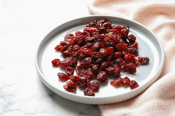 Plate with cranberries on marble table. Dried fruit as healthy snack
