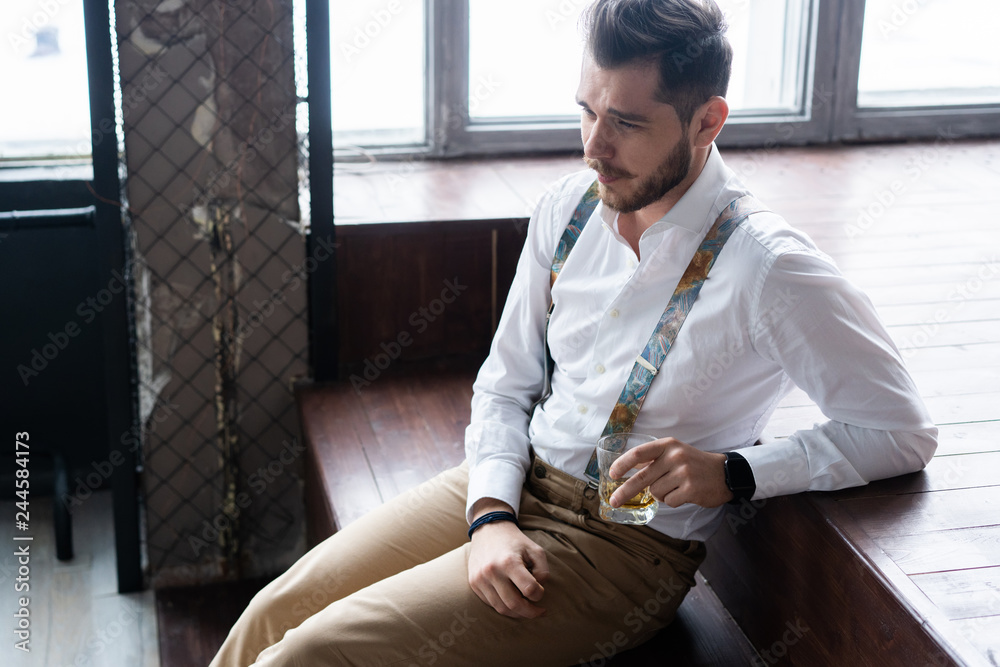 Wall mural feeling lonely. stylishly dressed young man holding a glass while sitting on sofa.