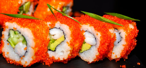 Eating Sushi with chopsticks. Sushi roll japanese food in restaurant. California Sushi roll set with salmon, vegetables, flying fish roe and caviar closeup. Japan restaurant menu