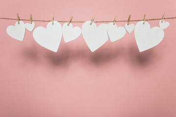 White love hearts pegged to a line against a pastel pink background - obrazy, fototapety, plakaty