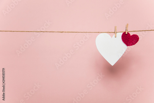 White and red love hearts pegged to a line against a pastel pink background