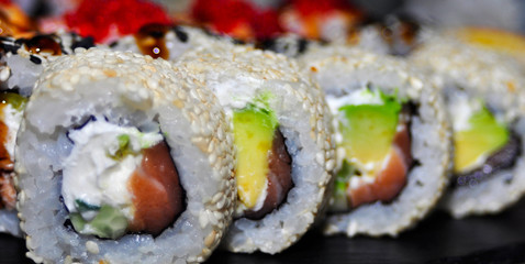 Eating Sushi with chopsticks. Sushi roll japanese food in restaurant. California Sushi roll set with salmon, vegetables, flying fish roe and caviar closeup. Japan restaurant menu