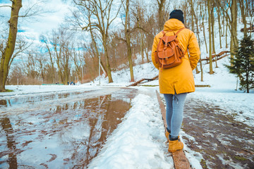 woman walking by city park passing puddles around. melting snow.