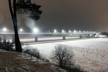 Bridge over the frozen river, lit by lanterns on a winter night