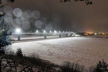 Bridge over the frozen river, lit by lanterns on a winter night with lens flares