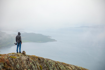 Fototapeta premium Young man looking on Panorama of nature view with fjord and mountains in clouds, Norway