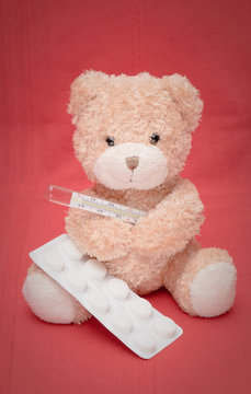 a teddy bear measures the temperature with a mercury thermometer and takes paracetamol tablets against high temperature